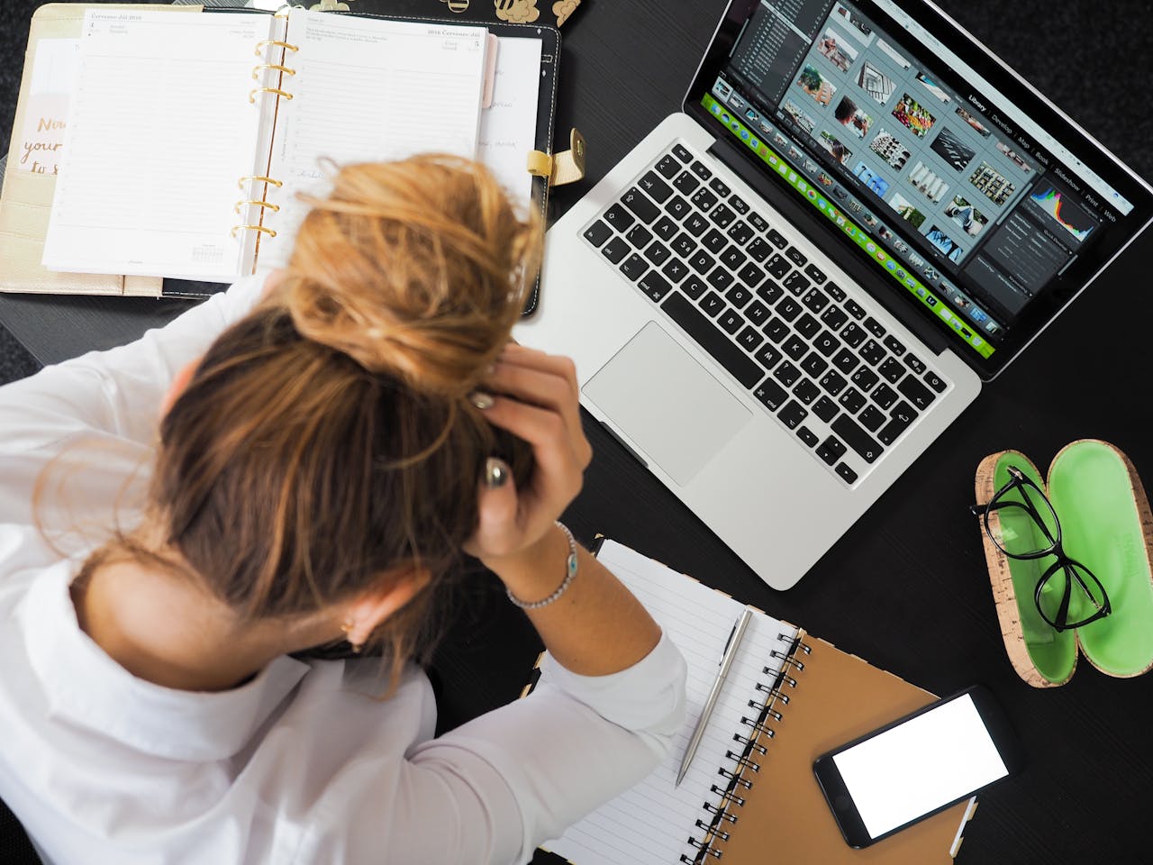 gallery-6 Overhead view of a stressed woman working at a desk with a laptop, phone, and notebooks.