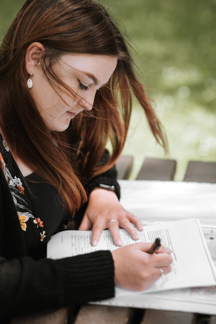 our-services-1 A young woman studies at an outdoor table in the park, focused and writing notes.