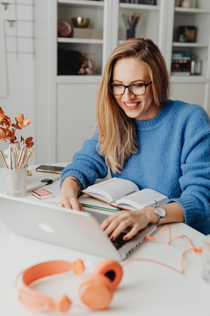 A cheerful woman in a blue sweater working remotely with a laptop in a cozy home setting.