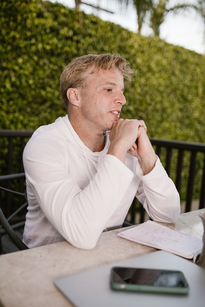 hero-img-02 Man seated outdoors in a casual setting using tech devices, captured in natural light.